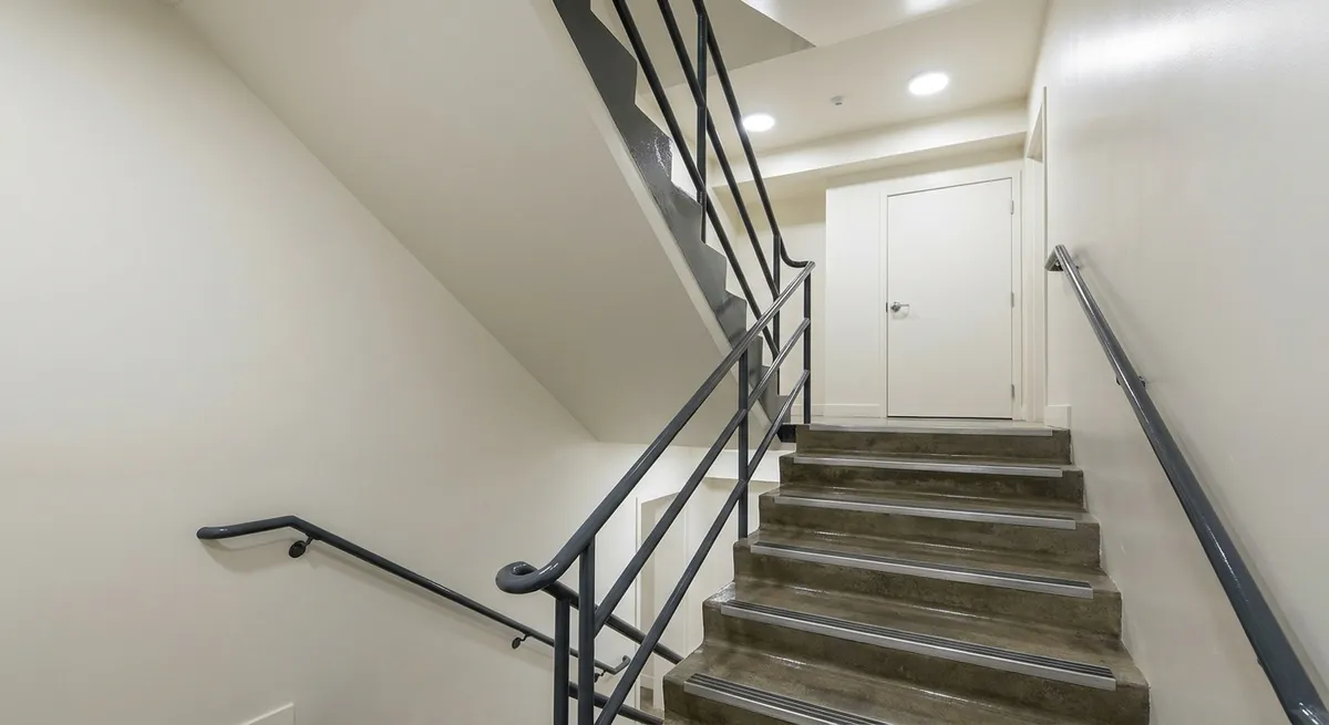 Escalera interior de un edificio con paredes blancas y barandal gris recién pintados